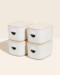 Four Open Spaces Medium Cream Storage Bins with wooden lids on a cream background. 