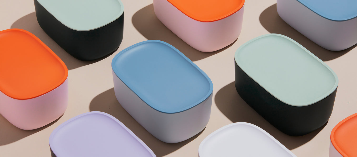 Different colored Small Storage bins with plastic lids on a cream background. 