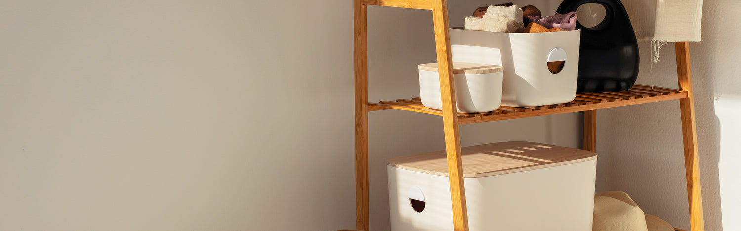 Different sized Opens Spaces cream with wooden lid storage bins on a wooden rack.