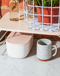 The Small Cream Storage Bin with a wooden lid under a shelf riser.