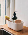 A Small Cream Storages Bins with dishwashing supplies in it on a wooden surface.