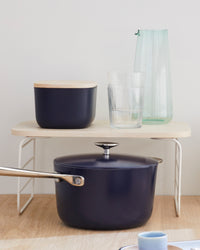 The Small Navy Storage Bin with a wooden lid on a shelf riser glasses and a cooking pot around it.