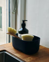 A Small Navy Storages Bins with dishwashing supplies in it on a wooden surface.