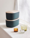 2 Dark Green Small Storage Bins next to candles on a white countertop.