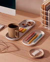 The Open Spaces Gray Nesting Tray with pens and other stationary on it on a wooden surface.