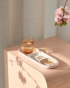 The Open Spaces Pink Nesting Tray with water and jewelry on it on a wooden surface.