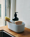 A Small Light Blue Storages Bin with dishwashing supplies in it on a wooden surface.