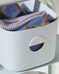 Close up of the Light Blue Medium Storage bin with cloths in it.