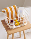 An Open Spaces Cream Medium Wire Basket with bath products on a wooden stool.