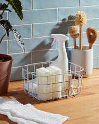 An Open Spaces Light Blue Medium Wire Basket with cleaning supplies on a wooden surface. 