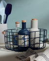 The Open Spaces Navy Medium Wire Basket with bottles inside it on a blue background.