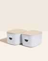 Two Open Spaces Light Blue Medium Storage Bins with wooden lids on a cream background.